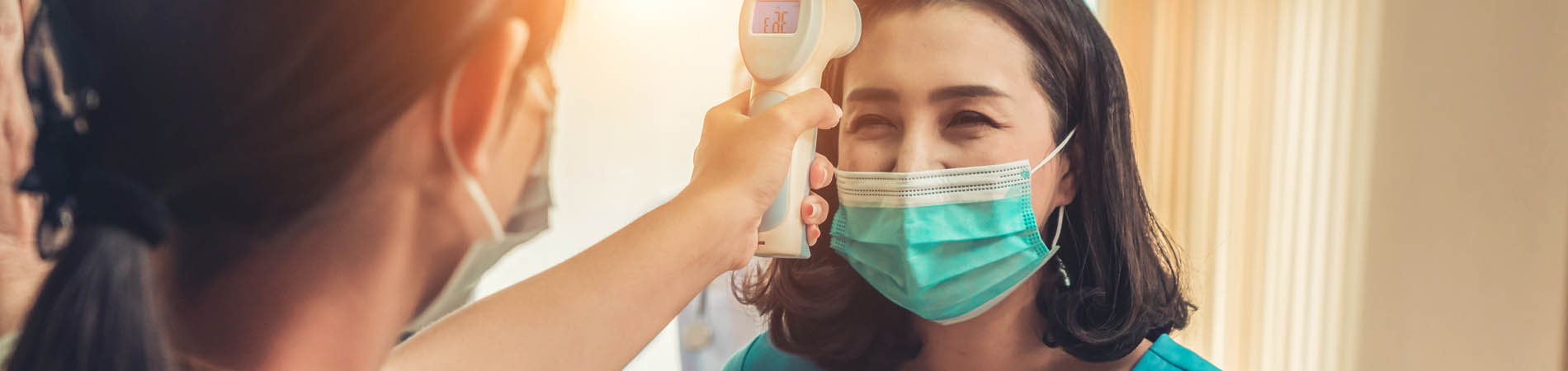 A medical front desk personnel taking the temperature of a patient on arrival